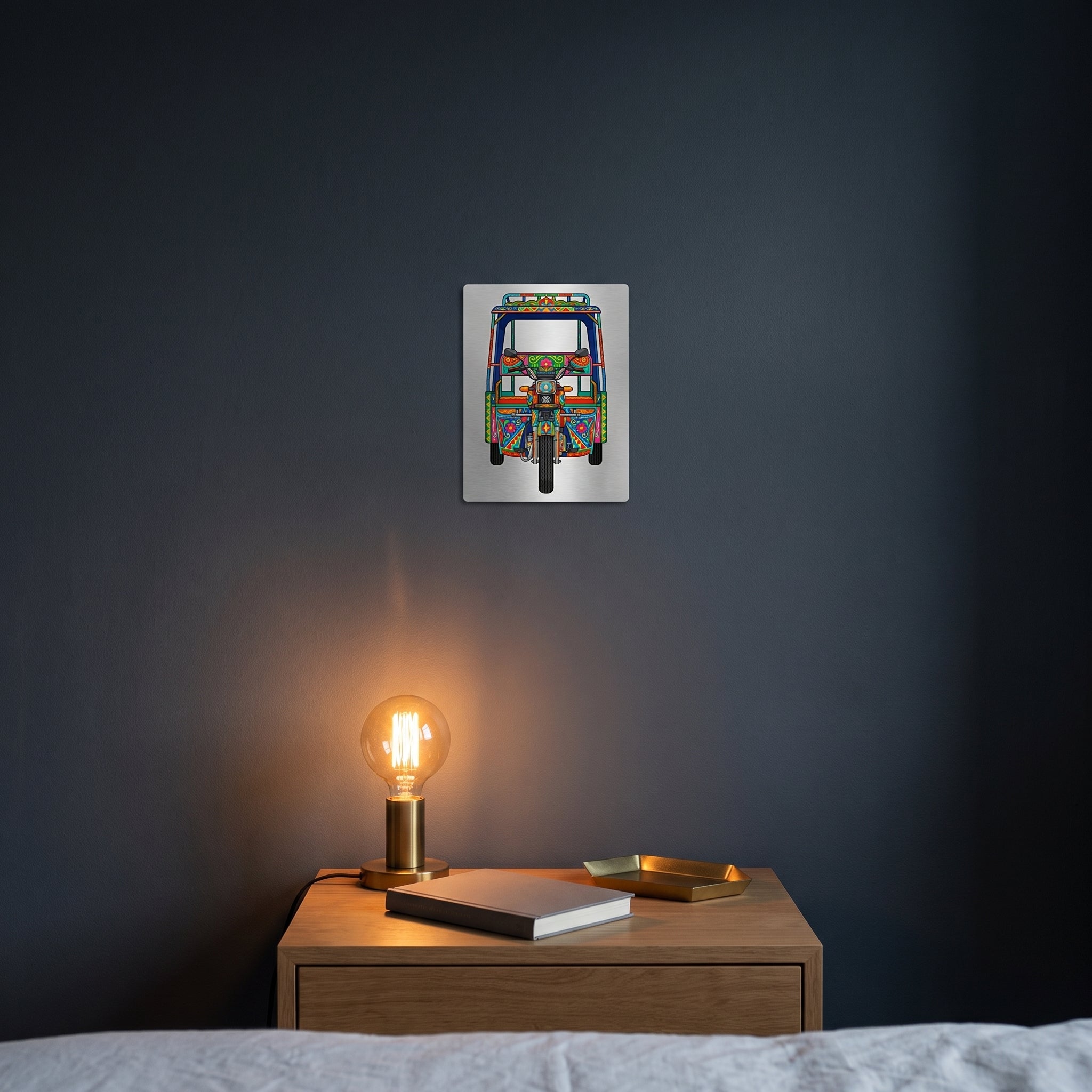 Pakistani motorcycle rickshaw art metal poster styled on a contemporary bedroom nightstand catching warm ambient light from a lamp.