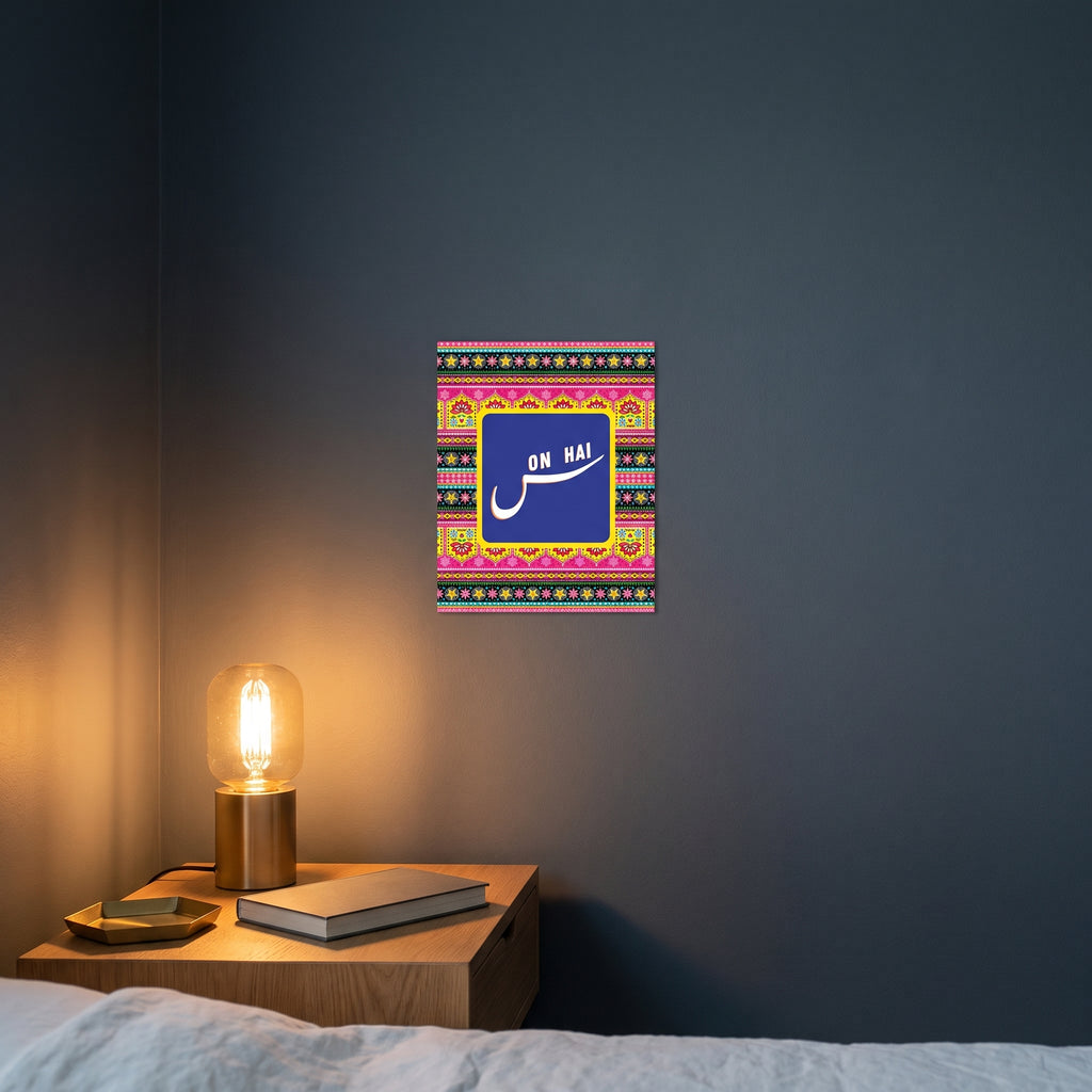 Pop-art style funny Desi phrase metal print catching warm ambient light from a lamp on a contemporary dark bedroom nightstand.
